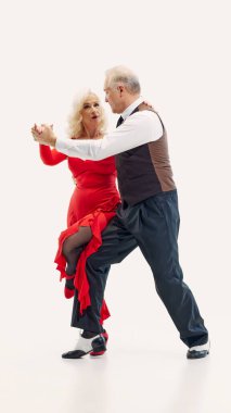 Elegant elderly couple, man and woman dressed in stylish matching dance costumes, dancing tango with passion and energy isolated on white background. Concept of retro dance, aging, active lifestyle clipart