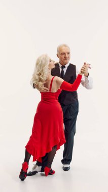 Elegant senior blonde woman in red dress and handsome senior man in black suit dancing tango isolated on white background. Concept of retro dance, hobby, aging, active lifestyle clipart