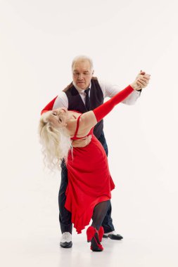 Full-length image of senior couple, man and woman dressed in elegant red dress and black classic suit, dancing tango isolated on white background. Retro dance, hobby, aging, active lifestyle concept clipart