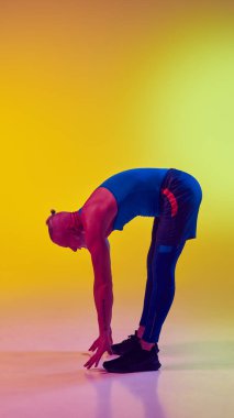 Spor giyimli yaşlı kaslı bir adamın, neonlu sarı arka planda eğitime karşı ısınma egzersizleri yaparken tam boy yan görünümü. Spor, aktif yaşlı yaşam tarzı, sağlık hizmeti konsepti