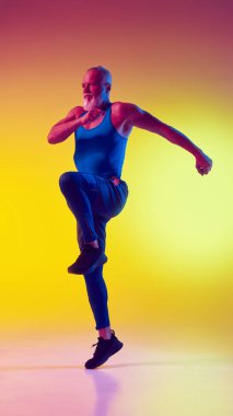 Spor giyimli yaşlı kaslı bir adamın hareketli dinamik görüntüsü, neon ışıkta eğimli sarı arka plana karşı antrenman yapıyor. Spor anlayışı, aktif yaşlı yaşam tarzı, sağlık hizmetleri