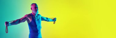 Güçlü eller. Kaslı vücutlu, spor giyimli yaşlı bir adam, neon ışıkta yeşil arka plana karşı direnç bandıyla antrenman yapıyor. Spor anlayışı, aktif yaşlı yaşam tarzı, sağlık