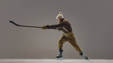 Sakallı bir adam, retro kıyafetli bir hokey oyuncusu, örgü şapka ve kazak giyiyor, pantolon pantolon askılı, stüdyo arka planında sopa ile hareket ediyor. Spor, oyun, turnuva, aksiyon, yarışma kavramı