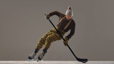 Kış sporları. Örgü kazak giyen, pantolon ve şapka giyen, çubukla buz pateni yapan, hokey oynayan bir adam. Spor, oyun, turnuva, aksiyon, yarışma kavramı