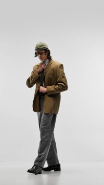 Şapkalı ve gözlüklü genç adam, çizgili ceket, gri pantolon ve beyaz stüdyo arka planında poz veren kravat. Klasik ve modern modanın karışımı. Moda kavramı, gençlik kültürü, şehir tarzı, reklam