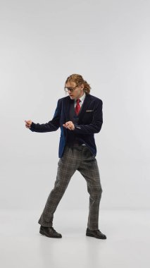 Lacivert kadife ceketli, kareli gri pantolonlu ve kırmızı kravatlı beyaz stüdyo arka planında poz veren şık bir genç. Moda anlayışı, gençlik kültürü, zarif tarz, reklam.