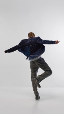 Lacivert kadife ceketli, kareli gri pantolonlu ve klasik siyah ayakkabılı, stüdyo arka planında hareketli bir gencin tam boy arka plan görüntüsü. Moda anlayışı, zarif tarz, reklam.