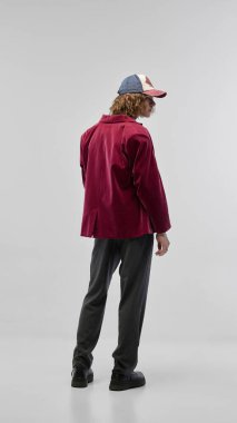 Kırmızı kadife ceketli, gri pantolonlu ve sıradan şapkalı genç bir adam. Beyaz stüdyo geçmişine karşı poz vermek. Moda kavramı, gençlik kültürü, şehir tarzı, reklam