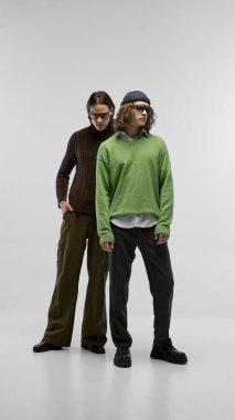 Stüdyonun arka planında poz veren, desenli süveter ve moda aksesuarlar giyen iki şık genç adam. Gençlik modası ve modern tarzlar. Moda kavramı, gençlik kültürü, şehir tarzı, reklam