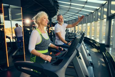Yaşlı bir adam ve kadın, canlı bir spor salonunda koşu bandı egzersizi yapan bir çift. Aktif ve sağlıklı kalmak için motivasyon. Yaşlıların konsepti, spor, aktif yaşam tarzı, sağlık