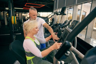 Spor salonunda sabit egzersiz bisikletiyle çalışan yaşlı çift. Yetişkinler için sağlık, spor ve ortak aktiviteler. Yaşlıların konsepti, spor, aktif yaşam tarzı, sağlık