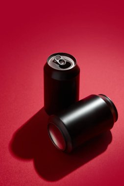 İki siyah alüminyum içecek kutusu, soda, bira ya da enerji içecekleri için, kırmızı arka planda dramatik gölgeler bırakarak. Minimalist ve çarpıcı bir görüntü. İçki markaları ve reklamlar için bir model.