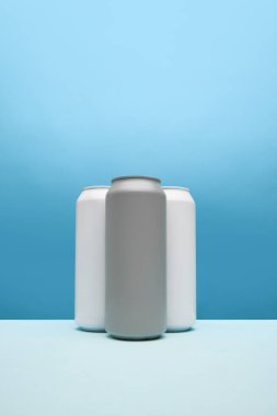 Üç şık, minimalist gri ve beyaz teneke kutu, mavi arka planda. Bira için maket, gazoz reklamı. Ürün markalaşması için basit ve şık bir temel. İlan için alanı kopyala