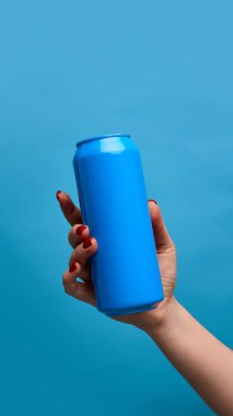 Mavi teneke giyen kadın açık mavi arka plana karşı. Modelleme. Bira, limonata, enerji içecekleri, kokteyller, soda. Ürün markalaşması için basit ve şık bir temel. İlan için alanı kopyala.