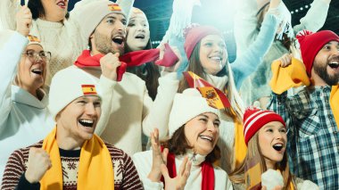 Bir grup sporsever, İspanyol takımını doldurulmuş stadyumda bayraklar ve eşarplarla kutluyor ve kış sporlarının şenlikli atmosferinin tadını çıkarıyorlar. Spor, oyun, rekabet, duygu kavramı