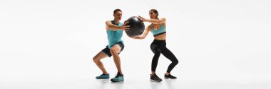 Sportif genç adam ve kadınlar birlikte antrenman yapıyor, beyaz stüdyo geçmişine karşı ilaç topuyla egzersiz yapıyorlar. Spor anlayışı, aktif ve sağlıklı yaşam tarzı, egzersiz, fitness. Banner, reklam