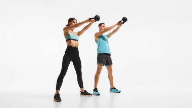 Sportif vücutlu, eğitimli, beyaz arka planda kettlebell ile egzersiz yapan genç bir erkek ve kadının tam boy görüntüsü. Spor anlayışı, aktif ve sağlıklı yaşam tarzı, egzersiz, reklam
