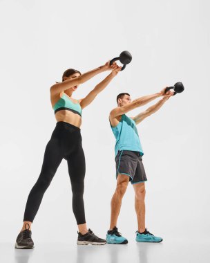 Sportif genç çiftin geniş açılı düşük açılı görüntüsü beyaz stüdyo arka planında kettlebell ile antrenman yapan kadın ve erkek. Spor anlayışı, aktif ve sağlıklı yaşam tarzı, egzersiz, fitness