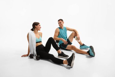 Genç adam ve kadın yerde oturuyor, su içiyor ve beyaz stüdyo arka planında yoğun bir eğitimden sonra dinleniyorlar. Spor, aktif ve sağlıklı yaşam tarzı, egzersiz, spor konsepti