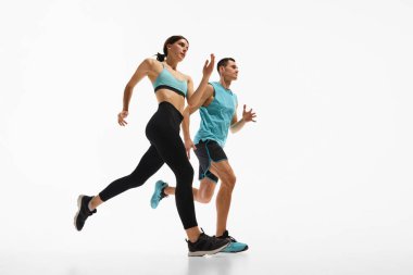 Genç atletik kadın ve kaslı adamın hareketli, eğitimli, beyaz stüdyo arka planına karşı koşan düşük açılı görüntüsü. Spor anlayışı, aktif ve sağlıklı yaşam tarzı, egzersiz, fitness