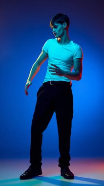 Üstü açık giyinen, beyaz tişörtlü, siyah pantolonlu, mavi ışıklı arka planda dans eden bir gencin uzun açılı görüntüsü. Gençlik kavramı, duygular, yaşam tarzı, moda