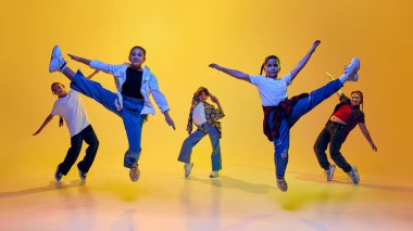 Şık ve hareketli genç kız, günlük kıyafetler içinde, dinamik bir şekilde dans ediyor, hip hop yapıyor, sarı arka planda neon ışıkta antrenman yapıyor. Modern dans kavramı, gençlik, aktif yaşam tarzı, hobi