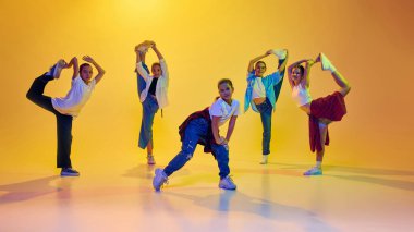 Esneklik ve yetenek. Bir grup genç kız hareketli şık kıyafetler içinde, neon ışıkta sarı arka planda hip hop dansı yapıyorlar. Modern dans, gençlik, aktif yaşam tarzı, hobi konsepti