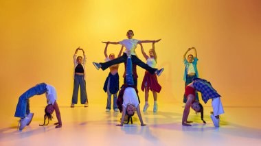 Bir grup yetenekli ve sanatsal genç kız, günlük kıyafetler giymiş gençler, neonlu sarı arka planda hip hop dansı yapıyorlar. Modern dans kavramı, gençlik, aktif yaşam tarzı, hobi
