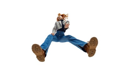 Akan kızıl saçlı, mavi kot pantolon giyen ve beyaz stüdyo arka planında bronz çizmeleri olan şık bir genç kadın. Alt manzara. Moda anlayışı, gençlik kültürü, yaşam tarzı, günlük giysiler.