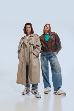 Büyük beden ceket giyen ve geniş bacaklı kot giyen iki genç kadın, beyaz stüdyo geçmişine karşı modern kıvrımlı retro-ilham verici kıyafetler sergiliyorlar. 90 'ların modası, eski moda, gençlik kavramı