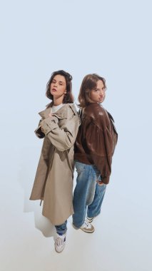 İki büyük beden ceket ve trençkot giyen iki genç kadın, beyaz stüdyo geçmişine karşı retro-esinlenmiş kıyafetler sergiliyorlar. 90 'ların modası, eski moda, gençlik kavramı