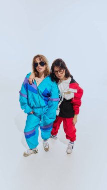 90 'ların kalın rüzgarlığı içinde iki kadın. Renkli eşofmanlar ve beyaz stüdyo geçmişine karşı poz veren moda gözlük. 90 'ların modası, eski moda, gençlik kavramı
