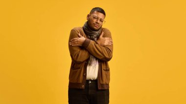 Atkı takmış Hintli bir adam ellerini sarıp sarmalamış, ateşten muzdarip, sarı stüdyo arka planında üşümüş ve hasta hissediyor. Hastalık, ilaç, tedavi, sağlık hizmetleri kavramı. Soğuk algınlığı