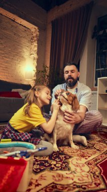 Bearded man in his 30s and young girl using toy medical set to treat their dog in playful and caring game at home in cozy living room. Concept of animal, childhood, parenthood clipart