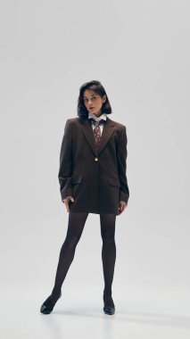 Genç güzel bir kadının tam boy portresi siyah tayt giyer, kahverengi büyük beden kravat takar ve stüdyo arka planında güvenle poz verir. İş anlayışı, moda eğilimleri, güzellik, tarz