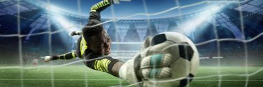 Parlak üniformalı kaleci, futbol topunu ağdan birkaç santim uzakta yakalamak için kolunu uzatıyor. Oyuncular ve stadyumun arka planında parlak ışıklar altında görülüyor. Spor, oyun, turnuva, yarışma kavramı