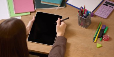 Tablet üzerinde çalışırken Stylus 'u tutan kadın, tahta masa üzerinde not defterleri, kalemler ve hesap makineleriyle çevrili, odaklanmayı ve teknolojiyi vurguluyor. İş kavramı, modern teknolojiler, dijital sanat