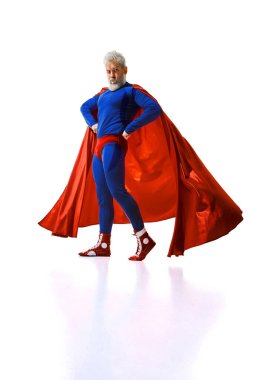 Gri saçlı, sakallı, kırmızı pelerinli, mavi süper kahraman kıyafetli, beyaz stüdyo geçmişine neşe saçan komik adam. Mizah anlayışı, parti, karnaval. Dergi kapağı, poster, reklam