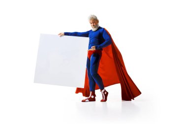 Süper kahraman kostümü giymiş gri saçlı adam beyaz stüdyo arka planında boş alanı olan büyük beyaz posterli boğa güreşçisi pozu veriyor. Duyuru, haber, reklam kavramı