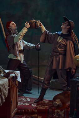 İki korsan, biri kırmızı bandana ve diğeri tüylü şapkalı, bira dolu ahşap bardaklar, klasik deniz donanımlı loş ışıklı odada içkinin tadını çıkarıyorlar. Macera kavramı, fantezi