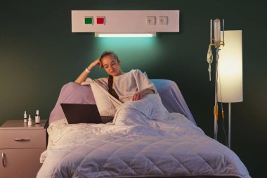 20 'li yaşlarda genç bir kadın hastanede yatıp dizüstü bilgisayarla yeşil duvarın karşısında film seyrediyor ve yanında yıldırım ve damlayan ekipmanlar var. Sağlık, ilaç, tedavi kavramı