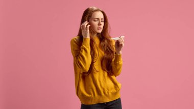 20 'li yaşlardaki genç bir kadın kendini hasta hissediyor, ateşi ölçüyor, pembe stüdyo arka planında mevsimlik soğuk algınlığı geçiriyor. Hastalık, ilaç, tedavi, sağlık