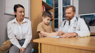 Pozitif hizmet. Anne ve doktor onunla ilgilenirken çocuk masaya not alıyor. Çocuklar için temel kontrol. Sağlık, ilaç, tedavi kavramı