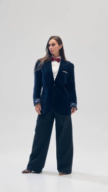 Uzun boylu, kadife takım elbiseli bir kadın resmi, büyük beden ceket ve pantolon, beyaz gömlek ve stüdyo arka planında kırmızı papyon. İş anlayışı, moda eğilimleri, güzellik, tarz