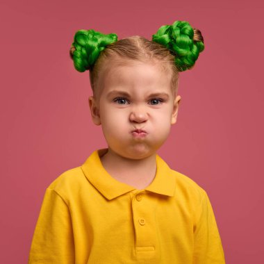 Kreş kızı portresi, sarı tişörtlü çocuk komik suratlar yapıyor, pembe stüdyo arka planına karşı suratını buruşturuyor. Çocukluk kavramı, duygular, yaşam tarzı, eğlence, eğlence