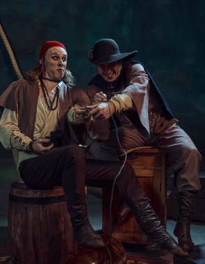 İki adam, ortaçağ korsanı, çevrimiçi video oyunlarına duygusal olarak karışmış, ellerinde kontrolörler ve oyunlar, karanlık vintage arka planla mücadele ediyorlar. Dönem, eğlence ve boş zamanlardaki karşılaştırma kavramı