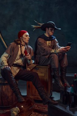 Genç erkekler, klasik kostümlü ortaçağ korsanları akıllı telefonlarla oturuyor, sosyal medyayı yönlendiriyor, loş ışıklı odada karanlık arka planla ilgili haberleri tartışıyorlar. Dijital ağ kavramı