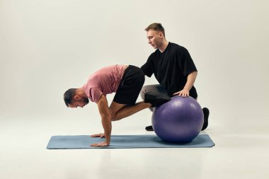 Antrenör, dengeli diz kapağı sıkıştırılmış bir adama yardımcı oluyor. Hafif stüdyo geçmişine karşı rehabilitasyon için çekirdek nişana odaklanıyor. Rehabilitasyon, iyileşme, sağlık, fizik tedavi