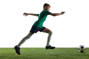 Yandan görünüşlü genç bir çocuk, yeşil formalı futbol katmanı ve çimenli zeminde hareket eden siyah gömlekli beyaz arka planda top sürüyor. Spor, eğitim, rekabet kavramı