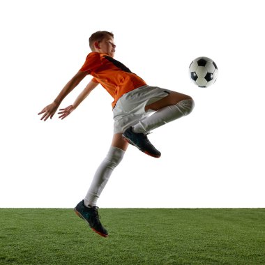 Odaklanmış, turuncu formalı, beyaz şortlu, diziyle topa vuran, beyaz arka planda antrenman yapan dinamik bir çocuk. Spor, eğitim, rekabet, oyun kavramı